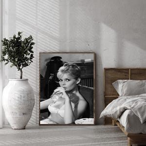Puede incluir: Impresi&oacute;n enmarcada en blanco y negro de una mujer en sujetador fumando un cigarrillo. La impresi&oacute;n se exhibe en un dormitorio, con una cama y un jarr&oacute;n decorativo. La imagen tiene una est&eacute;tica vintage.