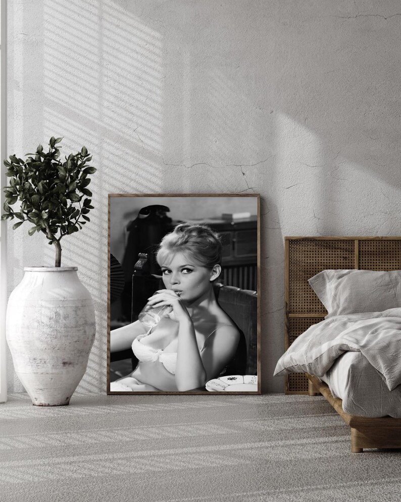 Puede incluir: Impresi&oacute;n enmarcada en blanco y negro de una mujer en sujetador fumando un cigarrillo. La impresi&oacute;n se exhibe en un dormitorio, con una cama y un jarr&oacute;n decorativo. La imagen tiene una est&eacute;tica vintage.