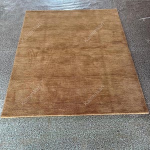 Puede incluir: Una alfombra rectangular marr&oacute;n con una superficie texturizada. La alfombra es de color liso y parece estar hecha de un material suave. La alfombra est&aacute; colocada sobre una superficie gris.