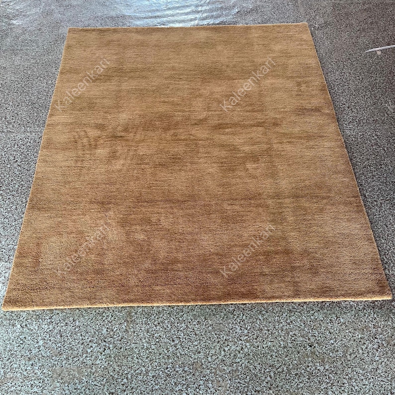 Puede incluir: Una alfombra rectangular marr&oacute;n con una superficie texturizada. La alfombra es de color liso y parece estar hecha de un material suave. La alfombra est&aacute; colocada sobre una superficie gris.