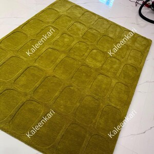 May include: A rectangular area rug in a solid chartreuse green color featuring a repeating embossed pattern of rounded rectangles across the entire surface. The word Kaleenkari is printed diagonally in white text across the rug in four locations.