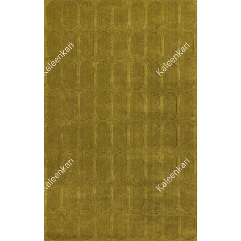 May include: A rectangular area rug in a solid mustard yellow color featuring a repeating pattern of embossed vertical oval shapes across the entire surface. The word Kaleenkari is printed in white text diagonally across the rug surface.