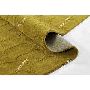 May include: A mustard yellow area rug featuring a repeating pattern of embossed oval shapes. The rug is folded over to reveal a light gray backing material. The word Kaleenkari is printed in white text across the surface of the rug.