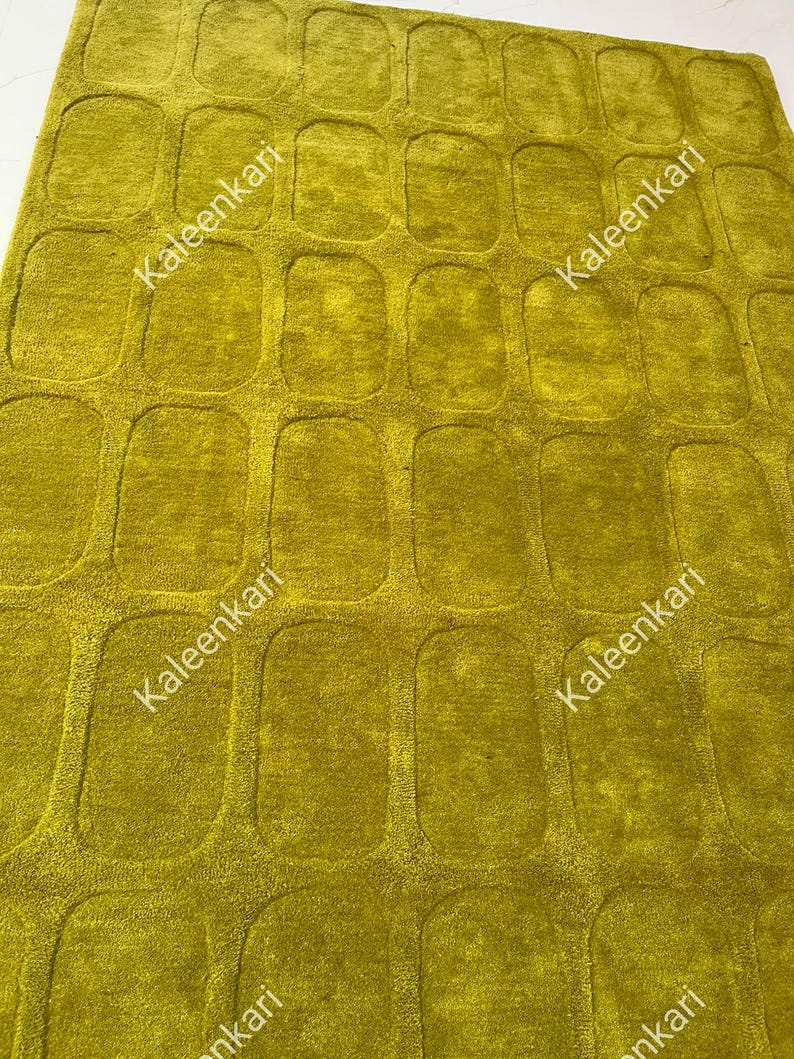 May include: A chartreuse area rug featuring a repeating pattern of raised, rounded rectangular shapes across the entire surface. The word Kaleenkari is printed in white text multiple times across the rug in a diagonal orientation.