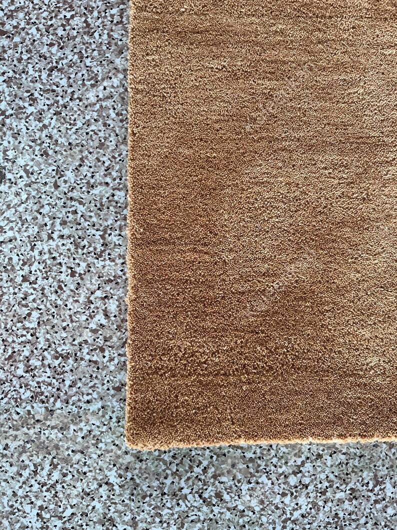 Puede incluir: Primer plano de una alfombra rectangular marr&oacute;n con superficie texturizada. La alfombra est&aacute; hecha de un material suave y tiene una textura ligeramente irregular. La alfombra se coloca junto a una superficie gris moteada.