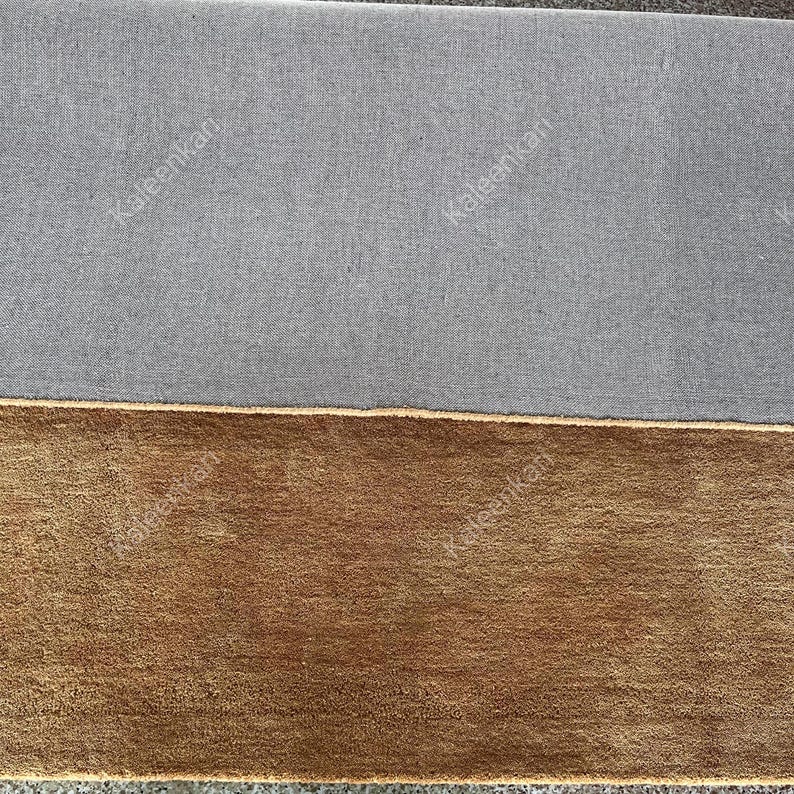 Puede incluir: Vista de cerca de dos alfombras rectangulares. La alfombra superior es de color gris liso, y la alfombra inferior es de color marr&oacute;n liso. El texto "Kaleenkan" est&aacute; impreso en ambas alfombras.