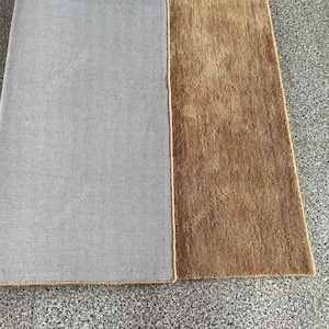Puede incluir: Primer plano de dos alfombras rectangulares. Una alfombra es de color gris liso y la otra es de color marr&oacute;n liso. Las alfombras est&aacute;n una al lado de la otra, con un borde beige. Las alfombras est&aacute;n sobre una superficie gris.