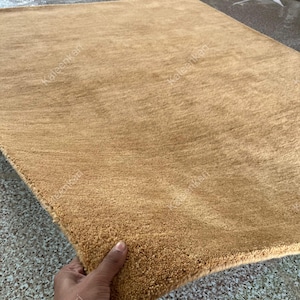 Puede incluir: Una alfombra rectangular de color marr&oacute;n dorado con una superficie texturizada. La alfombra parece suave y afelpada, con una vista de cerca que resalta el tejido detallado. La alfombra es de color neutro, adecuada para varios estilos de dise&ntilde;o de interiores.