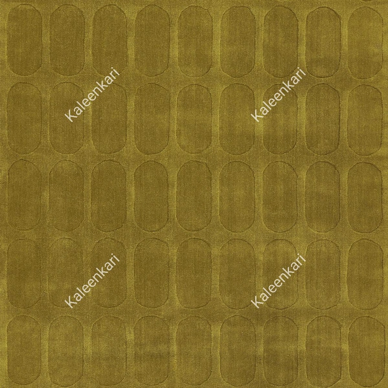 May include: A mustard yellow rug featuring a repeating pattern of vertical pill-shaped indentations across the entire surface. The text Kaleenkari is printed diagonally in white across the rug in two separate locations on the fabric.