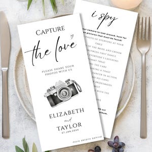 May include: Two white wedding cards with black text. One card reads "Capture the love" with a camera illustration. The other card says "i spy" with a list of photo prompts. The names Elizabeth and Taylor are printed on the first card.