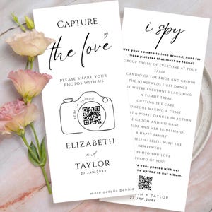 May include: Two white wedding cards with black text. One card says "Capture the Love" and includes a camera graphic with a QR code. The other card says "I Spy" and lists photo prompts. The names "Elizabeth and Taylor" are printed on the first card.