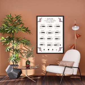 Peut inclure: Un poster encadré du calendrier lunaire Feng Shui 2026. L'affiche présente les phases de la lune pour chaque mois, avec des accents floraux. La pièce comprend une chaise moderne, une table d'appoint et une plante en pot.