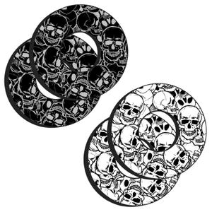 May include: Four black and white coasters with a skull pattern. The coasters are round with a circular cutout in the center. The skull design is repeated across the surface of each coaster.