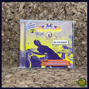 May include: A CD case featuring the album "The Weird Tapes No. 2" by Hawkwind. The cover art has a psychedelic design with purple and yellow hues, a silhouetted figure, and the text "Here is the unusual."
