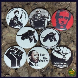 May include: A collection of round buttons with various designs and text. The buttons feature images of a Black Panther, a raised fist, and portraits of historical figures. Text includes "All Power to the People" and "Fulfill the dream."