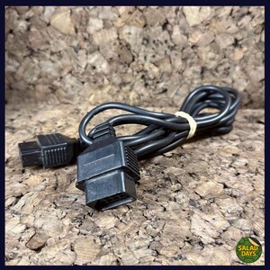 May include: A black video game console AV cable with two connectors and a long cord, bundled with a rubber band. The connectors are rectangular with multiple pins. The cord is coiled.