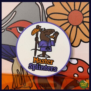 May include: A round, white sticker with a cartoon rat character in a purple gi, holding a pizza slice and a staff. The text "Master Splinters" is below the character in orange and purple. The background has floral and abstract designs.