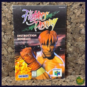 May include: Fighters Destiny instruction booklet for Nintendo 64. The cover features a muscular man with orange hair and a boxing glove, set against a fiery background. The game's title is in a stylized font, with the Nintendo 64 logo visible.