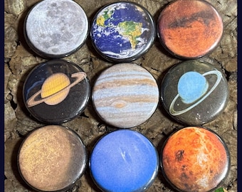May include: Nine round planet-themed buttons, each with a different planet design. The planets include Earth, Mars, Jupiter, Saturn, Uranus, Venus, and Neptune, along with the Moon. The buttons are arranged in a 3x3 grid.