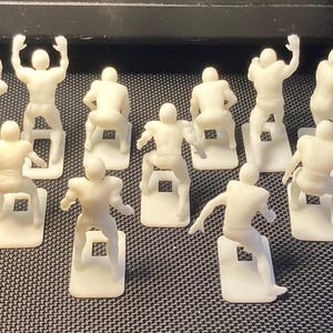 May include: A collection of off-white miniature football player figurines in various action poses. Each figure is mounted on a small, rectangular base. The figures are arranged on a dark surface.