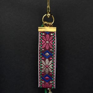 Back of bag charm featuring geometric floral embroidered ribbon in pink, blue, green, and beige tones.