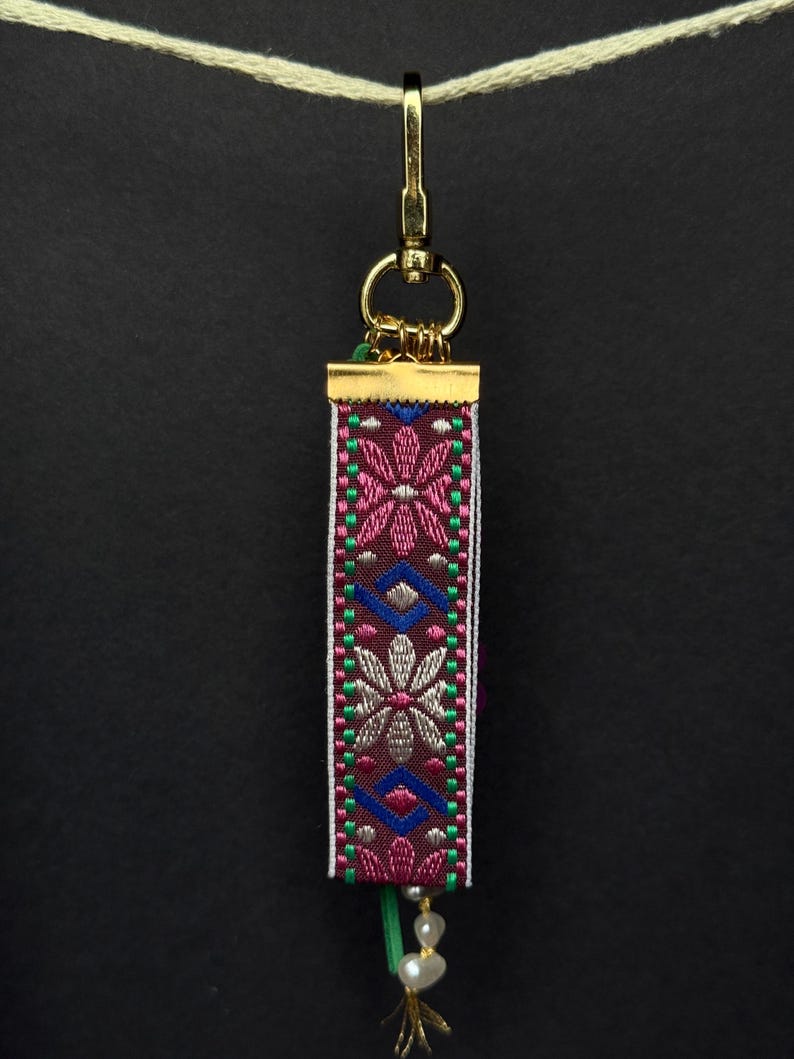 Back of bag charm featuring geometric floral embroidered ribbon in pink, blue, green, and beige tones.
