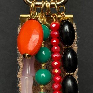 Close-up of top section showing faceted orange bead, black oval beads, red crystal beads, and green round beads hanging from gold rings.