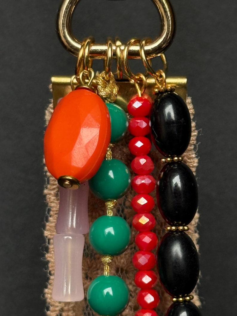 Close-up of top section showing faceted orange bead, black oval beads, red crystal beads, and green round beads hanging from gold rings.