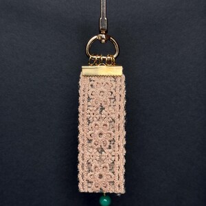 Back side of bag charm with beige floral lace ribbon and single green bead accent.