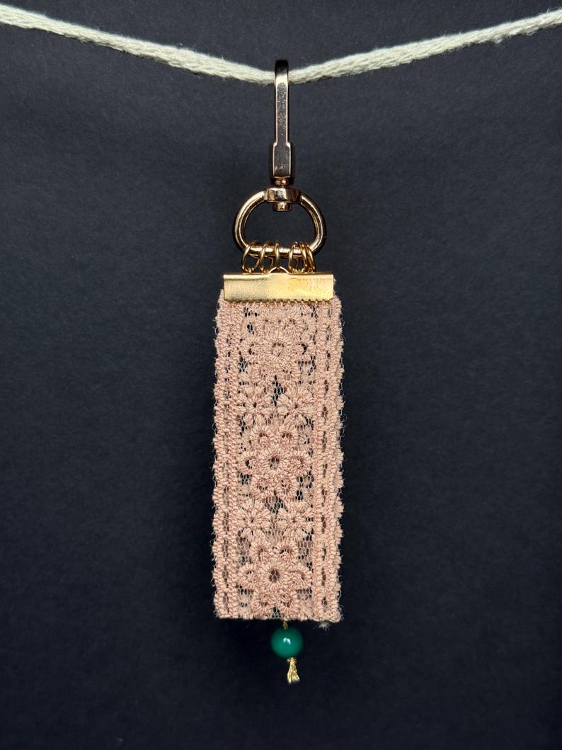 Back side of bag charm with beige floral lace ribbon and single green bead accent.