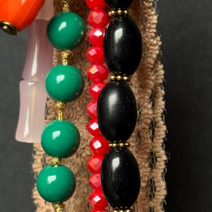 Macro view of black and red bead strands with gold details over beige lace fabric.