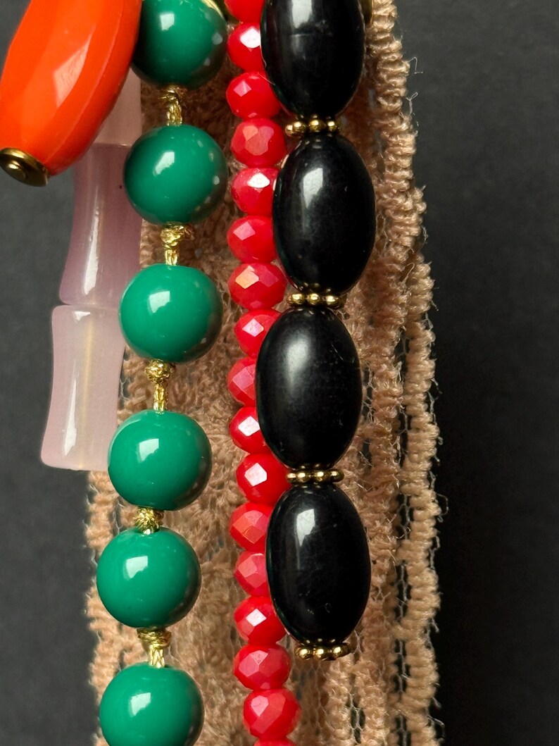 Macro view of black and red bead strands with gold details over beige lace fabric.