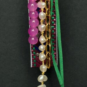Lower section of charm showing pearl and pink beads hanging alongside a green suede strip and gold chain.