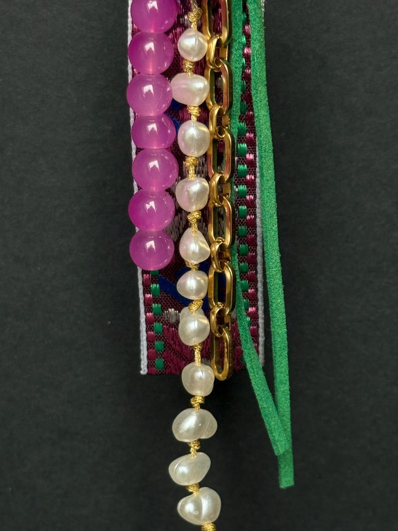 Lower section of charm showing pearl and pink beads hanging alongside a green suede strip and gold chain.