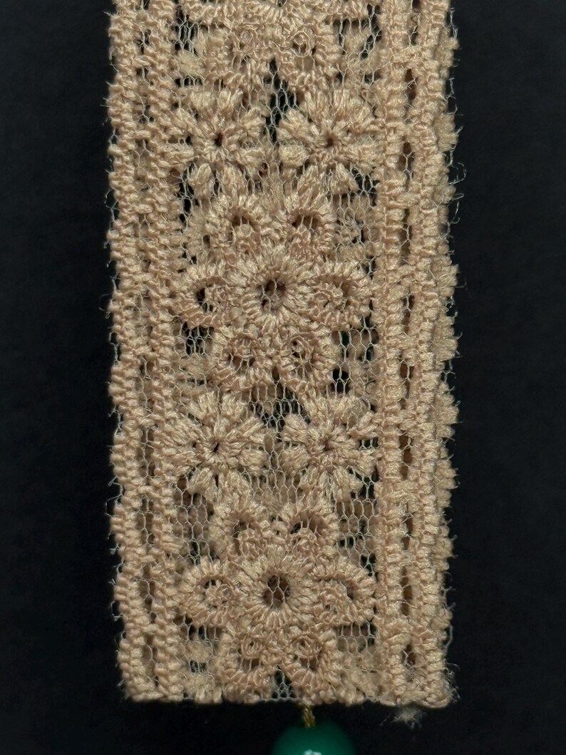 Close-up of intricate beige lace ribbon showing delicate floral embroidery pattern.