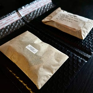 May include: Two sealed bubble mailers with adhesive strips, one black and one with a brown paper package. The brown package has a label that says "STUDIO TUTTEBELLO". A smaller package has "Care tips" printed on it.