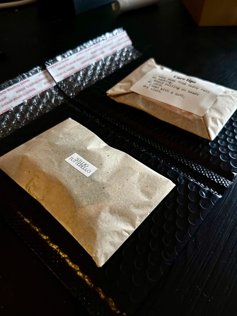 May include: Two sealed bubble mailers with adhesive strips, one black and one with a brown paper package. The brown package has a label that says "STUDIO TUTTEBELLO". A smaller package has "Care tips" printed on it.