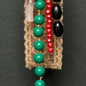Detailed view of turquoise-green bead strand and pink glass pieces hanging from textured lace ribbon.