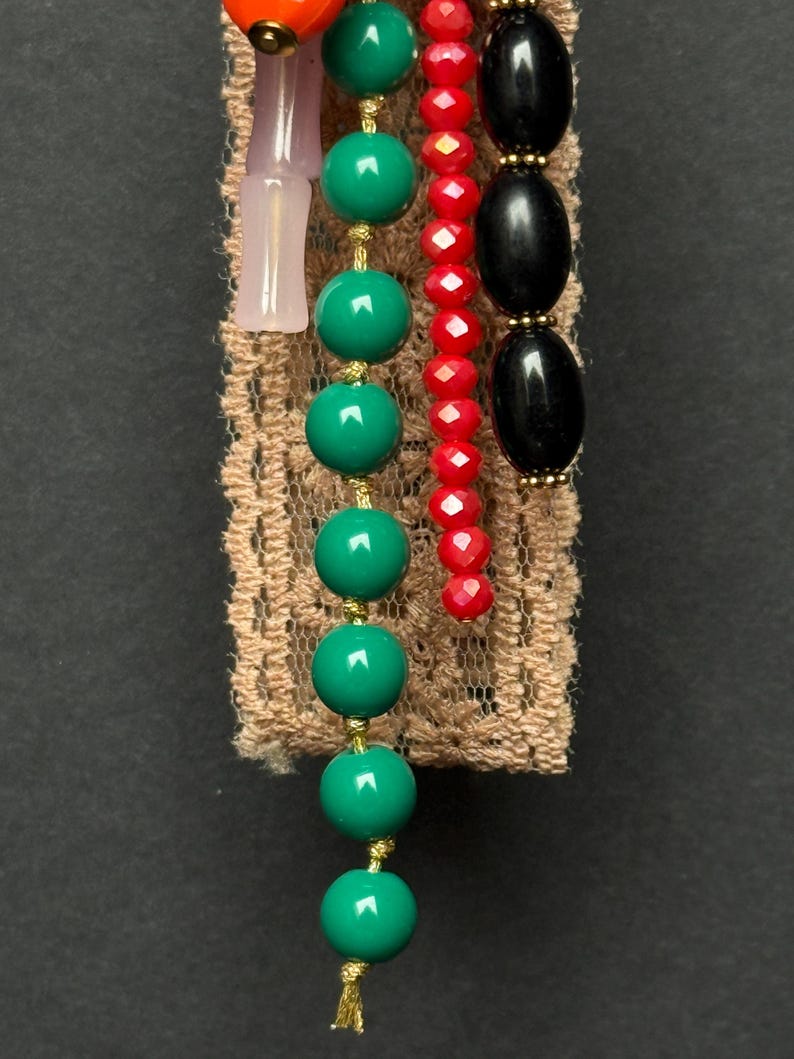 Detailed view of turquoise-green bead strand and pink glass pieces hanging from textured lace ribbon.