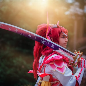 May include: A person in a pink and white costume with a red wig and a sword with a purple and white blade. The sword has white flowers on it.