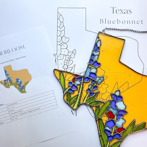 May include: A stained glass suncatcher shaped like the state of Texas, featuring yellow glass and bluebonnet flowers in shades of blue, red, and green. The piece includes a dark metal chain and is displayed over a printed Texas Bluebonnet pattern sheet.