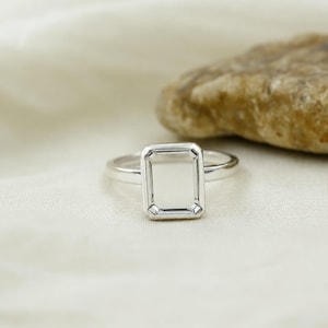 May include: A polished silver ring featuring a rectangular, flat-topped bezel setting. The band is smooth and circular, connecting to a clean, geometric frame that holds a flat, reflective silver surface in the center of the ring head.