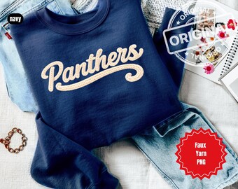 May include: Navy blue sweatshirt with the word "Panthers" in a cream-colored, textured font. The sweatshirt is folded on top of a pair of blue jeans. A small gold chain bracelet is visible. The word "navy" is in a black box.