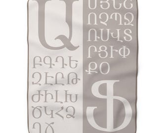 May include: A rectangular blanket with a two-tone design. The left side is white, and the right side is gray. Large gray Armenian letters are printed on the white side, and white letters are on the gray side. The blanket has a brown border.