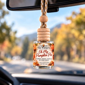 Puede incluir: Un frasco difusor de coche de vidrio con tapa de madera y cordón trenzado. La etiqueta presenta el texto The Wickery, Oh My Pumpkin Pie, Pumpkin, Spices, Vanilla, Buttery Crust, Car Diffuser y Net Wt. 8 ml, decorado con ilustraciones de calabazas.