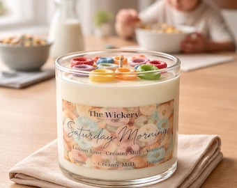 Könnte beinhalten: Ein Glas-Kerze mit cremeweißem Wachs, verziert mit bunten Cerealien. Das Etikett lautet "The Wickery Saturday Morning" mit Duftnoten. Ein Dekorationsartikel für den Haushalt.