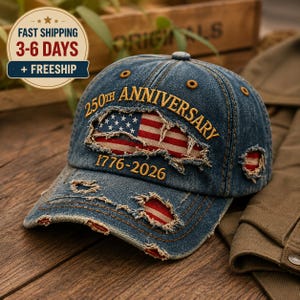 May include: A distressed blue denim baseball cap featuring the embroidered text 250TH ANNIVERSARY and 1776-2026. The cap has frayed cutouts revealing a red, white, and blue American flag pattern underneath the fabric on the front and side panels.