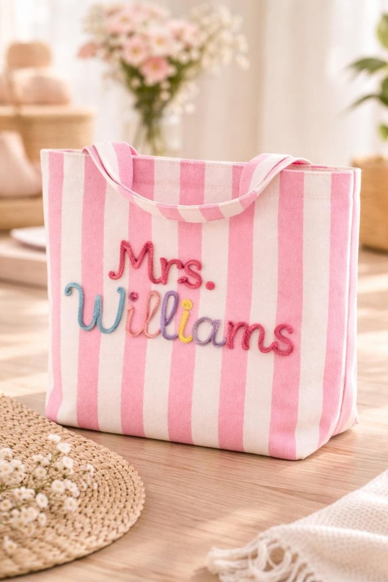 May include: A pink and white striped tote bag with the embroidered name "Mrs. Williams" in colorful thread. The bag has matching pink handles and is made of a sturdy fabric. The bag is a perfect accessory for carrying essentials.
