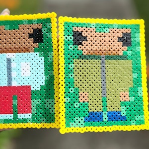 Puede incluir: Dos posavasos cuadrados de pixel art. Uno presenta una figura con camisa azul claro, pantalones cortos rojos y cabello castaño. El otro tiene una figura con camisa verde y pantalones azules. Ambos tienen bordes amarillos y están hechos de cuentas de colores.