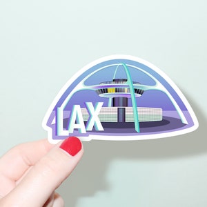 May include: A sticker featuring a stylized illustration of the iconic LAX airport terminal building in Los Angeles, California. The sticker is white with a purple and blue illustration and the text "LAX" in white.